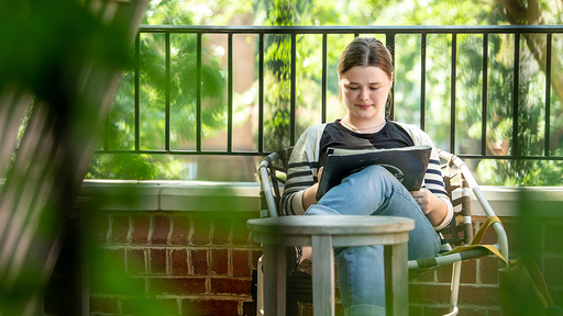 A student reviews coursework while sitting in the shade under the Founders Patio gazebo.