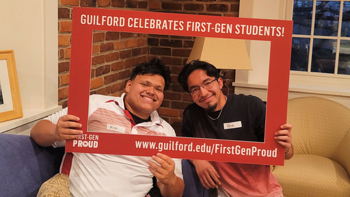 Two students take a selfie with a large frame that reads, Guilford Celebrates First-Gen Students!