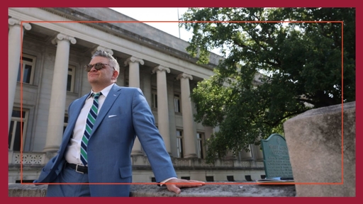 Michael Working '98 stands outdoors in front of a courthouse, wearing a blue suit and white shirt.