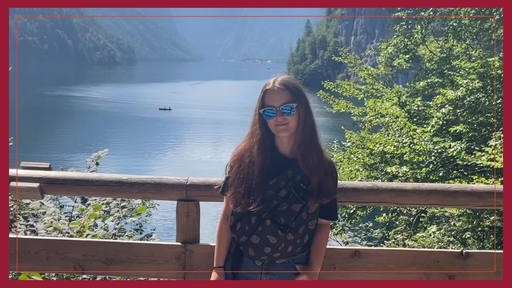 Maddie Smiley stands on a bridge in front of a lake wearing a short sleeve shirt and sunglasses.