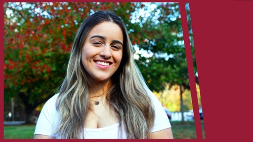 Kami Gonzalez stands outdoors with her long hair down, wearing a necklace and a white shirt, while smiling.