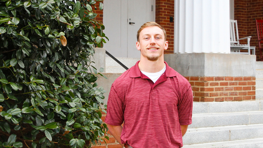 Eric Mays, class of 2022, stands in front of New Garden Hall in a red polo shirt