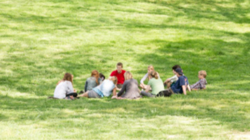 Students and a child gather in a circle on a sunny Guilford College campus lawn.