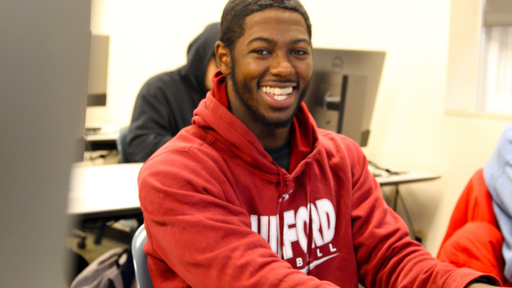 A Guilford College student sitting in a classroom smiling for a photo.
