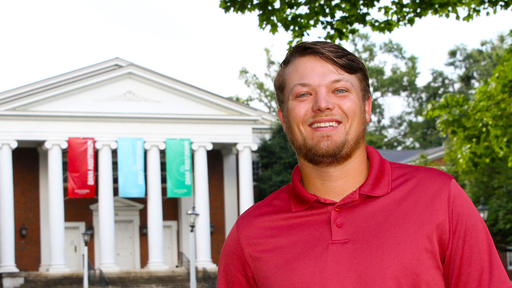 Jacob Cutshall inm a red polo, standing in front of Dana Auditorium