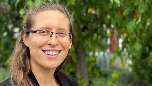 Smiling woman with glasses outdoors on Guilford College campus.