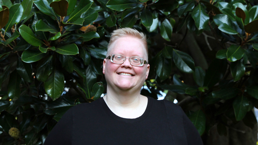 Heather Hollandsworth in black, standing in front of a Magnolia tree on campus