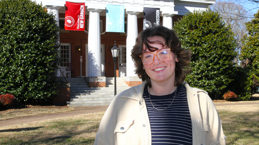 Liv Henderson wearing a tan jacket, standing in front of New Garden Hall