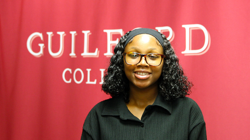 Tiana Chamberlain-Archie in black in front of a Guilford College banner