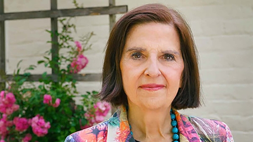 Guilford College President Jean Parvin Bordewich in a colorful jacket in front of Rachel's Rose Cottage