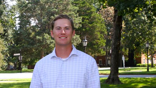 Aaron Williams in a light gray plad shirt, standing in the College Quad