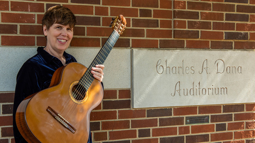 KAmi Rowan with her guitar, in front of the cornerstone for Dana Auditorium, where she often teaches and performs