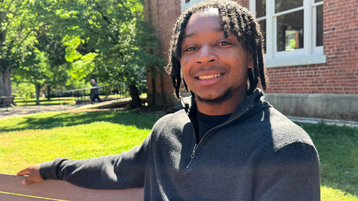 Smiling Guilford College student with dreadlocks on campus, bright sunny day.
