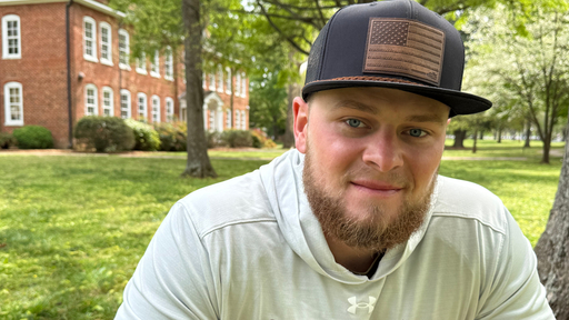Smiling man in American flag cap on Guilford College campus with brick building.