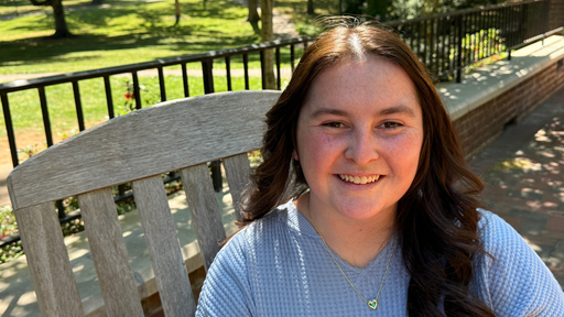 Smiling young woman sitting on a wooden bench on Guilford College campus.