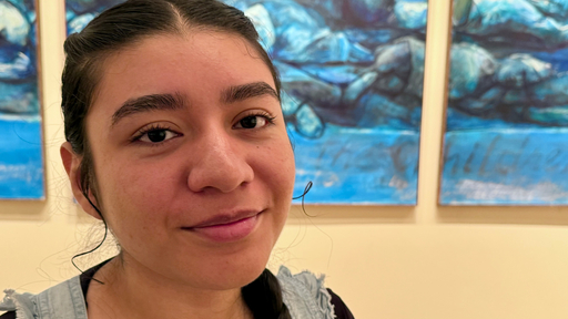Young person with dark hair smiling at the camera, abstract blue paintings behind them, possibly at Guilford College.