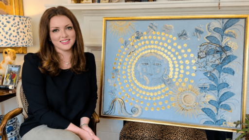 Photograph: Smiling woman next to a large painting with blue face, gold circles, suns, and foliage.