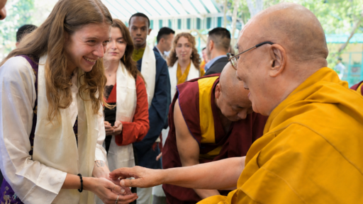 Smiling Guilford College student in white and purple respectfully greets the Dalai Lama in yellow robes.