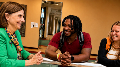 Smiling Guilford College staff member and two diverse students interacting.