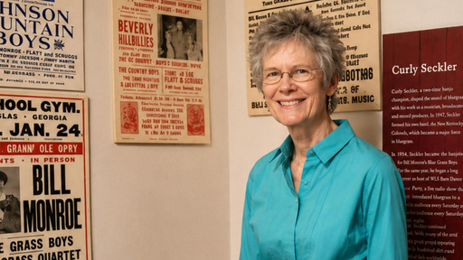 Smiling woman in a teal shirt, standing amidst vintage bluegrass posters at Guilford College.