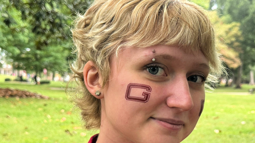 Young person with a "G" tattoo on their cheek smiles on Guilford College campus.
