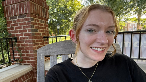 Smiling student outdoors on Guilford College campus, brick building and trees behind her.