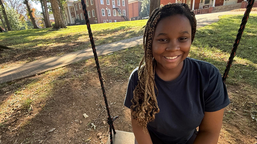 Smiling student on a swing with Guilford College campus buildings in background.