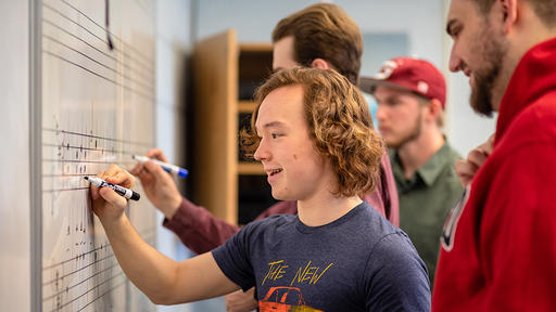 Music theory students practice writing notes at the white board.